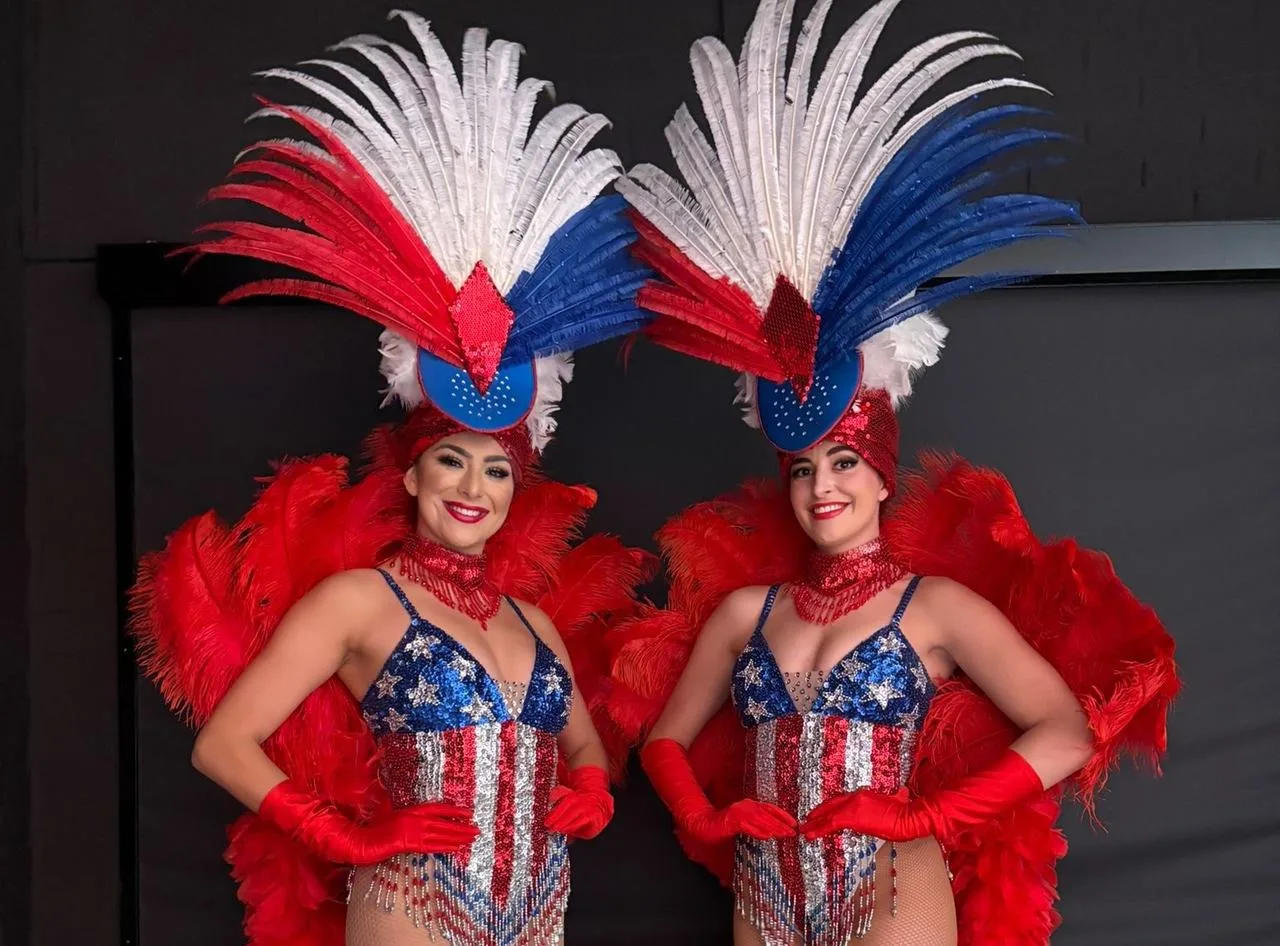 Two Vegas showgirls in stars and stripes costumes with red and blue feather headdresses